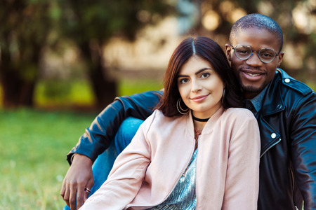 Portrait of Lovely multicultural couple sitting on a grass in the park and looking at camera  の写真素材
