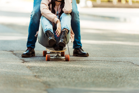 Cropped image of girlfriend sitting on a longboard and her boyfriend standing closeの写真素材