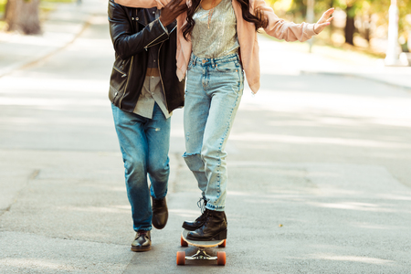 Cropped image of Boyfriend helping his girlfriend to skate on a longboard in the park  の写真素材