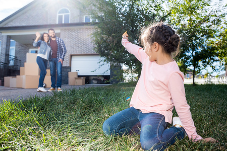 little girl waving to parents while sitting on grass of new gardenの写真素材