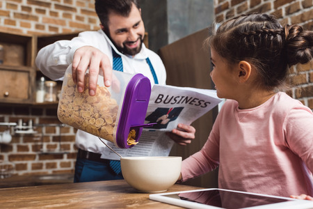 father making cereal breakfast for daughter while he talking by phone