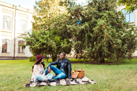 Lovely multicultural couple sitting on a blanket at the park の写真素材