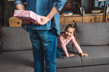 father hiding gift for excited little daughter behind backの写真素材