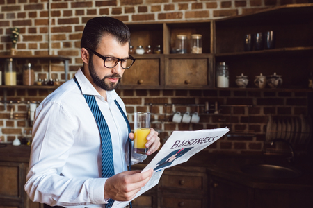 businessman reading newspaper and drinking fresh orange juice at kitchen in morningの写真素材