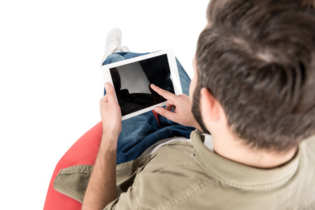 rear view of man using digital tablet while sitting on bean bag chair, isolated on whiteの写真素材