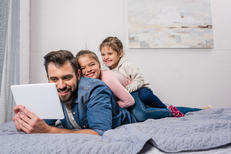 happy young father and daughters relaxing on bed with digital tabletの写真素材
