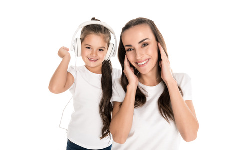 portrait of smiling mother and daughter in headphones looking at camera isolated on whiteの写真素材