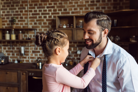 little daughter buttoning shirt for father on kitchenの写真素材