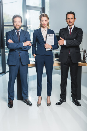 lawyers with arms crossed standing near colleague that holding contract in officeの写真素材