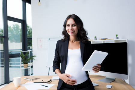 pregnant businesswoman with tablet at modern office looking at cameraの写真素材