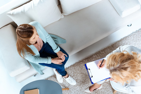 overhead view of psychotherapist writing on clipboard while young patient sitting on couchの写真素材