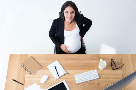 top view pregnant businesswoman with call center headset at workplaceの写真素材