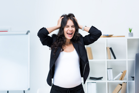pregnant businesswoman screaming and holding head with handsの写真素材
