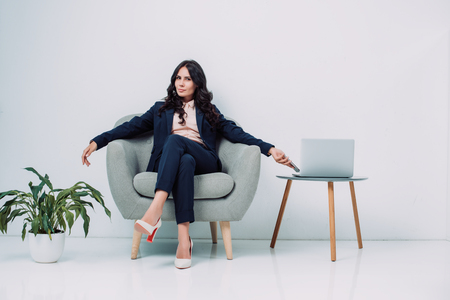 beautiful young businesswoman relaxing in armchair with laptop on tableの写真素材