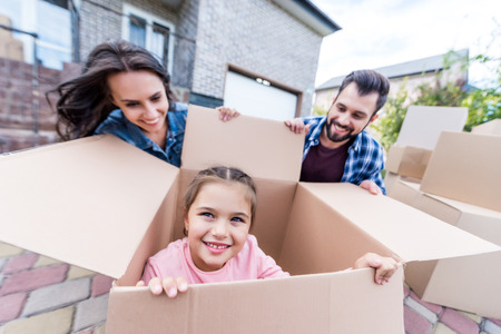adorable little girl sitting in cardboard box while happy parents looking at herの写真素材