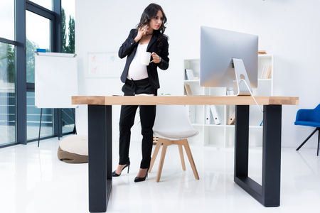 serious pregnant businesswoman talking by phone at workplaceの写真素材