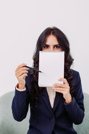 young businesswoman covering face with blank notepad and pointing at itの写真素材