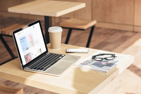 laptop with ebay website, smartphone and business newspaper on table in coffee shopのeditorial素材