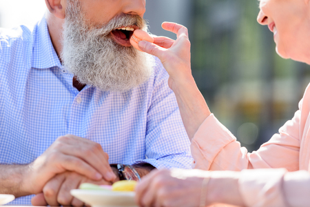 cropped shot of woman feeding senior man with sweet macaroonの写真素材