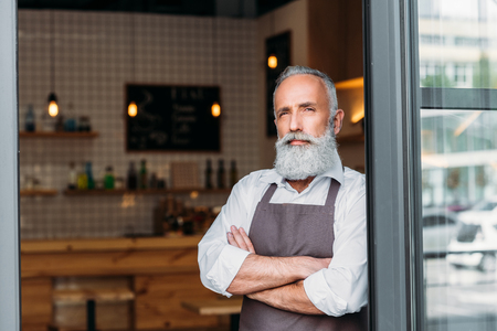 portrait of pensive senior coffee shop worker in apron looking awayの写真素材