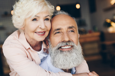 portrait of smiling senior woman hugging husband in cafe