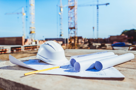 Rolls of paper with building plans and hardhat on wooden surface at construction site