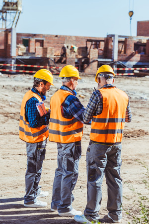 Three workers in hardhats and reflective vests standing at construction siteの写真素材