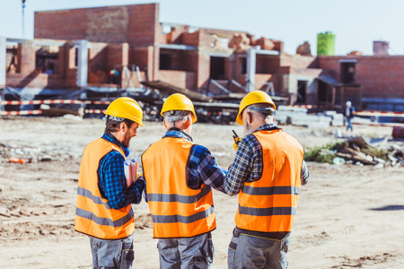 Three workers in hardhats and reflective vests standing at construction siteの写真素材
