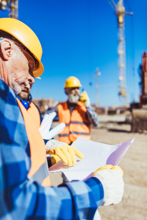 Foreman examining a building plan while standing at construction site with colleaguesの写真素材