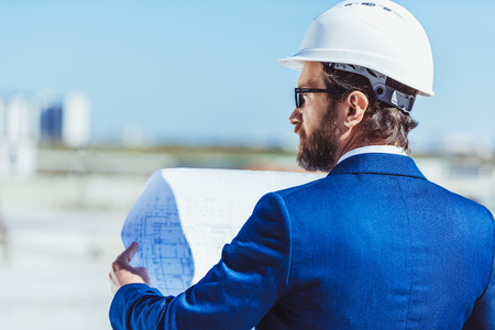 Businessman in hardhat and suit examining building plansの写真素材