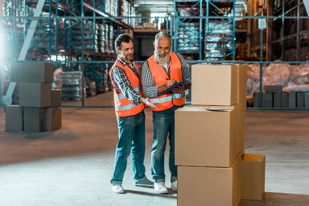 two male warehouse workers writing on clipboard and looking at boxesの写真素材