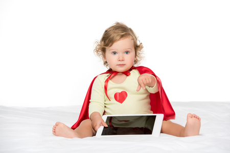 adorable toddler in superhero cape with tablet pointing isolated on whiteの写真素材