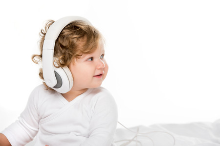 portrait of smiling toddler listening music in headphones isolated on whiteの写真素材