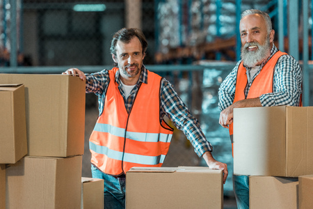 cheerful warehouse workers standing with boxes and smiling at cameraの写真素材