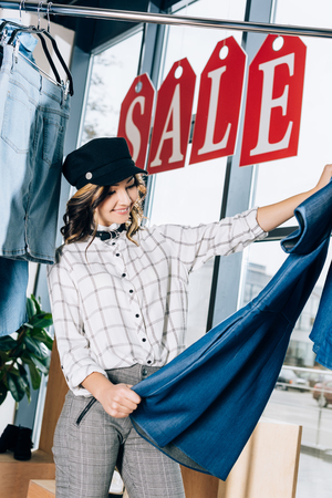 stylish young woman looking at blue denim dress at clothing storeの写真素材