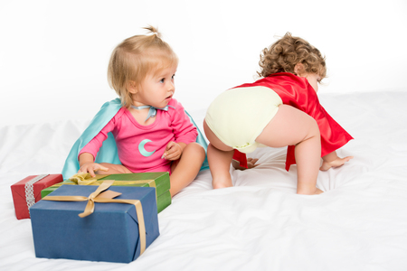 adorable toddlers in superhero capes with wrapped gifts isolated on whiteの写真素材