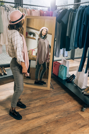 happy young woman looking at mirror in clothing storeの写真素材