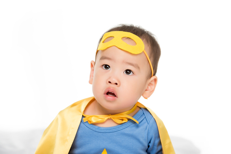 portrait of adorable asian toddler boy in superhero cape and mask isolated on whiteの写真素材