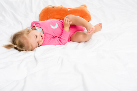 smiling baby in bodysuit with toy near by lying on bedの写真素材