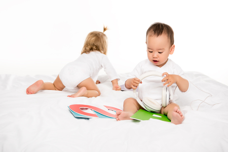 asian toddler boy holding headphones while girl crawling behind isolated on whiteの写真素材