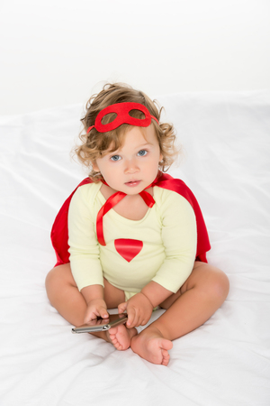adorable toddler girl in superhero costume with smartphone isolated on whiteの写真素材