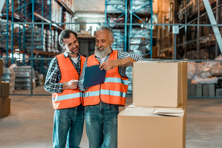 two smiling workers looking at clipboard while working in warehouseの写真素材