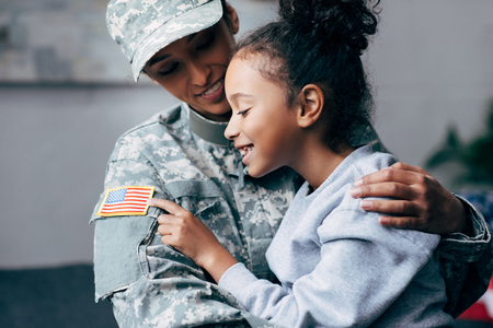 african american daughter hugging mother in military uniform at homeの写真素材