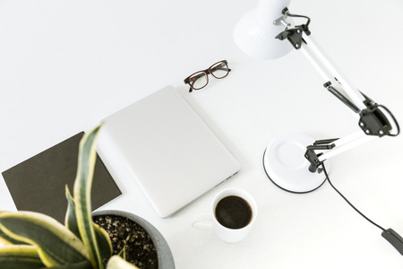 Composition with laptop, desklamp, glasses and cup of coffee on white tabletopの写真素材