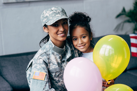 african american daughter and mother in military uniform with balloons at homeの写真素材