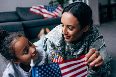 african american daughter and mother in military uniform with american flag at homeの写真素材