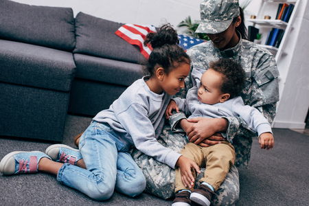 african american mother in military uniform sitting on floor with her little son and daughter  の写真素材