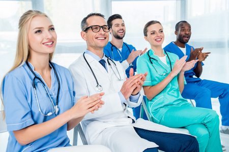 team of doctors sitting on chairs and clapping hands while listening to lectureの写真素材