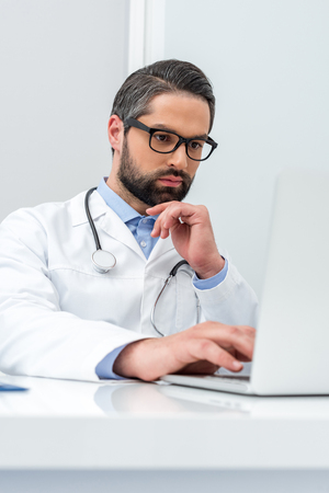 handsome thoughtful doctor using laptopの写真素材