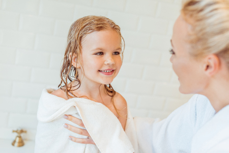 selective focus of mother holding towel and looking at cute happy daughter after bathの写真素材